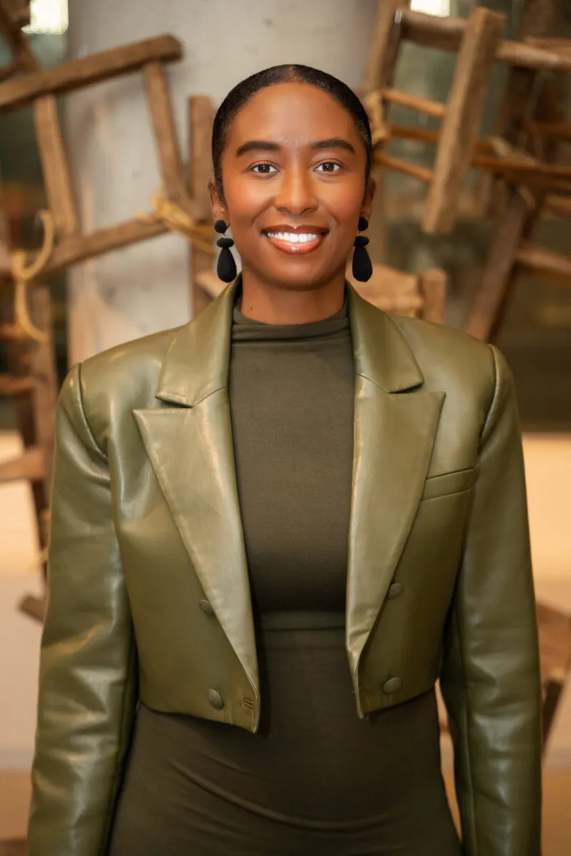 Portrait of Stephanie Johnson-Cunningham, Co-Founder and Executive Director of Museum Hue, a Black woman facing the viewer straight on with her hair pulled back and wearing large black dangling earrings with an olive green jacket and high-necked top